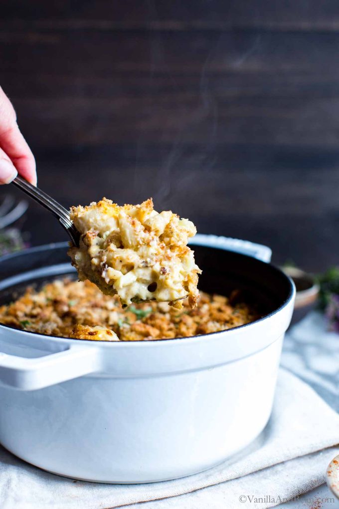 Baked mac and cheese with cauliflower being scooped up from a Dutch oven with steam rising off the mac and cheese.