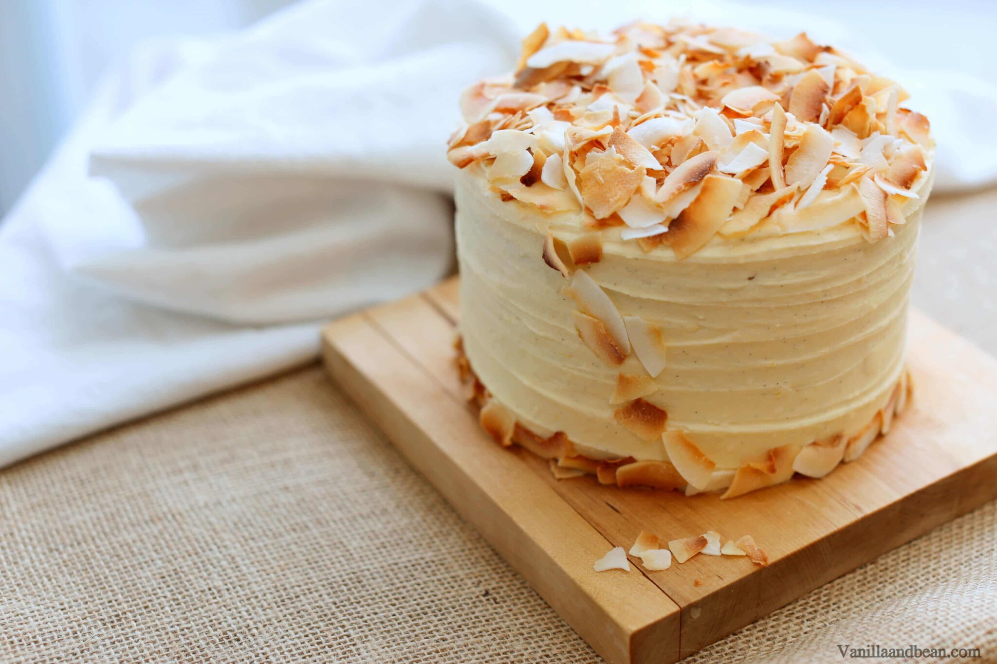 Hummingbird Cake topped with coconut flakes setting on a cake board.
