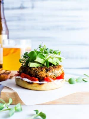Sweet Potato Burger topped with avocado and sprouts, setting on a cutting board ready to eat.