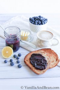 Blueberry jam in a small jar and some of the jam spread on a toasted bread.