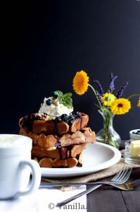 A close up of the waffles topped with blueberries, cream and syrup.