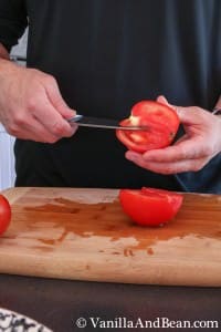 Cutting a tomato and half and removing the white area around the stem