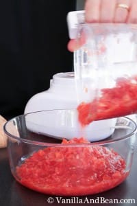 Pouring the tomatoes from a food processor into a large glass bowl