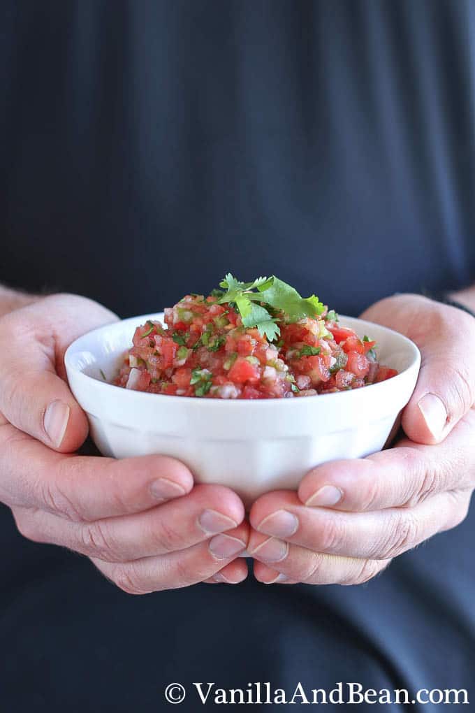 Two hands holding a small bowl of pico de gallo