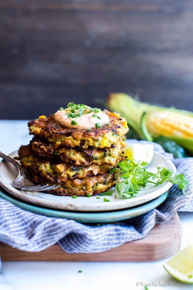 Zucchini Corn Fritters stacked tall on a plate with chipotle cream. 