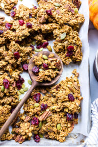 Baked crunchy pumpkin granola in a pan with a spoon holding some granola.