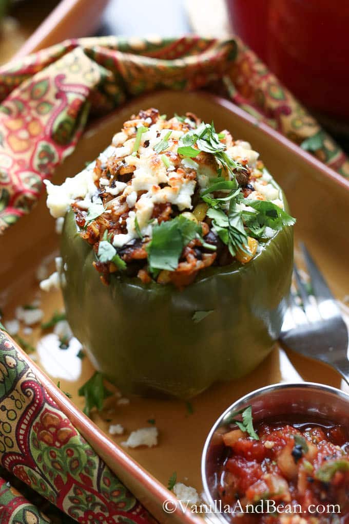 A stuffed green bell pepper and a very small bowl of salsa served in a casserole dish
