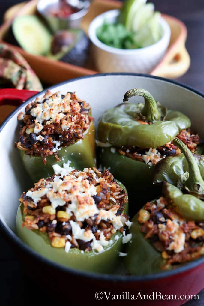 Placed in a round casserole dish are roasted peppers stuffed with brown rice, beans, veggies and cheese