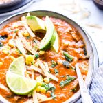 A bowl of creamy vegetarian tortilla soup garnished with lime wedges, avocados and tortilla strips.