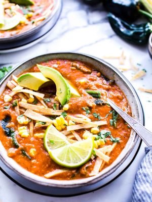 A bowl of Mexican Tortilla Soup garnished with lime wedges, avocados and tortilla strips.