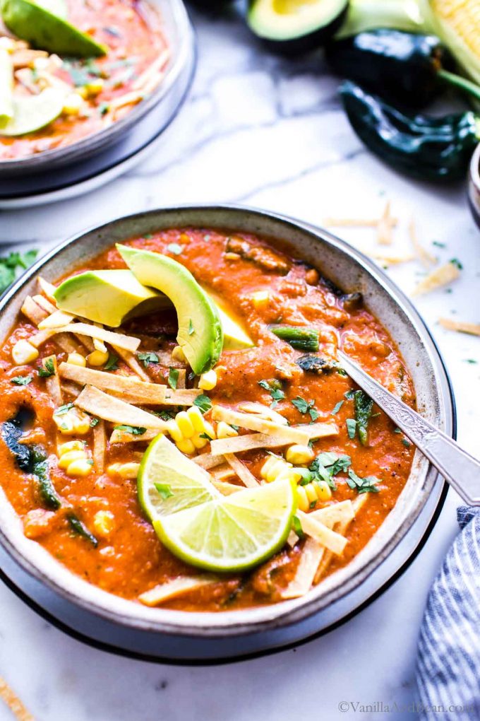 A bowl of Mexican Tortilla Soup garnished with lime wedges, avocados and tortilla strips. 