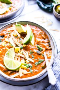 A bowl of creamy vegetarian tortilla soup garnished with lime wedges, avocados and tortilla strips.