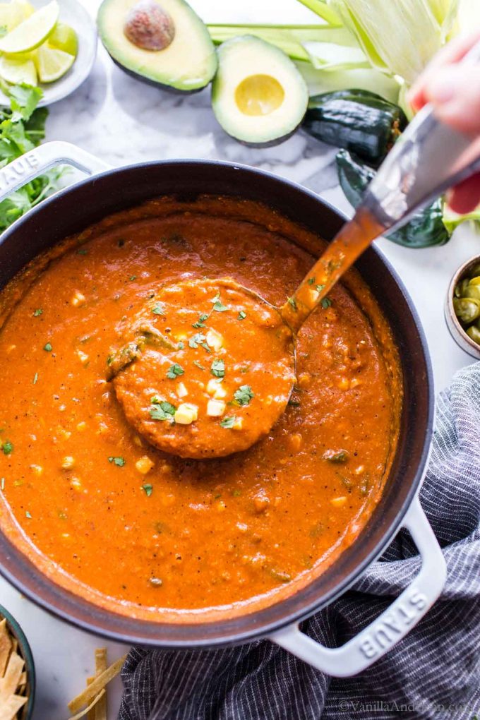 A Dutch oven full of of healthy vegan tortilla soup with a ladle scooping some up.