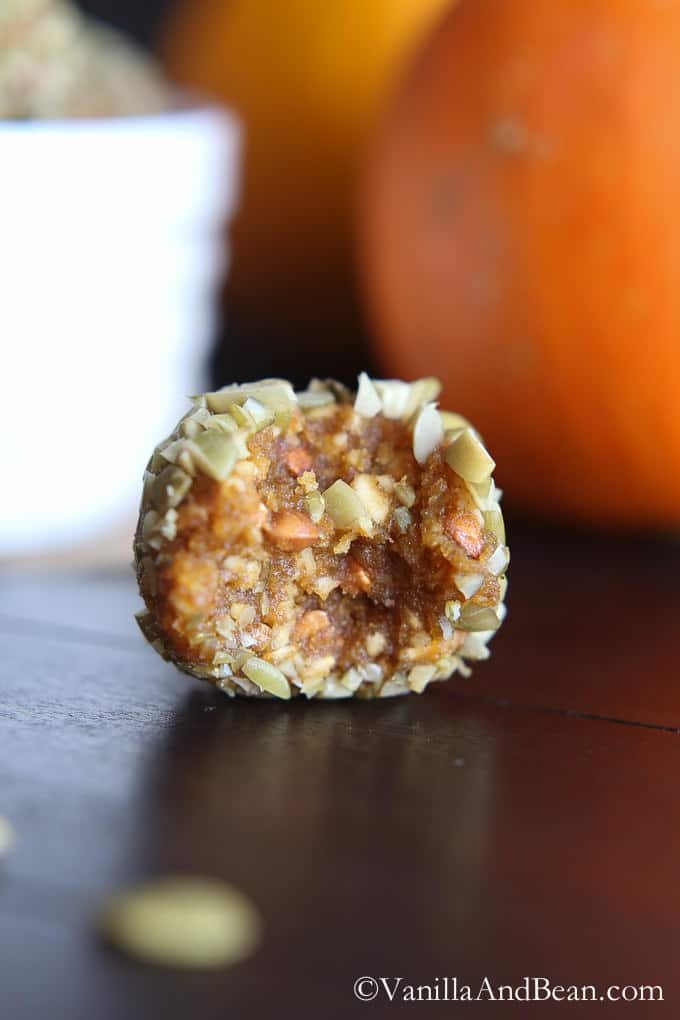 Half of a pumpkin kasha energy bite covered with finely chopped pepitas is placed on a table.