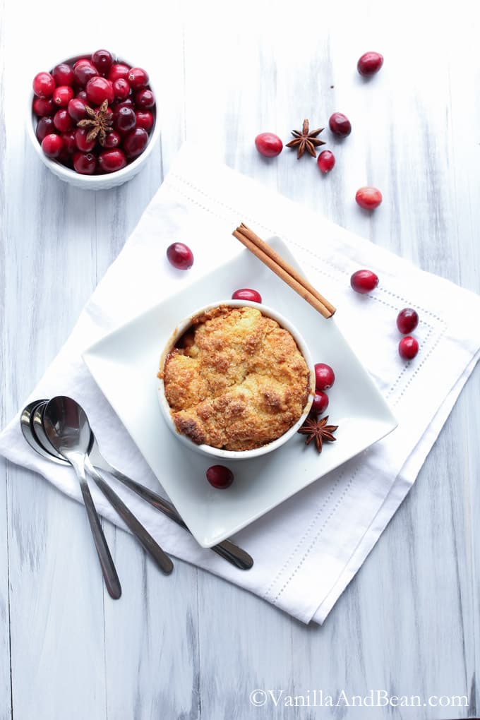 Bourbon Apple Cranberry Cobbler in a ramekin and fresh cranberries in a small bowl and some around the ramekin.