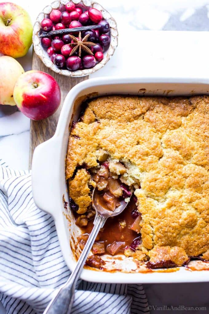Cranberry apple cobbler in a baking dish with a spoon.