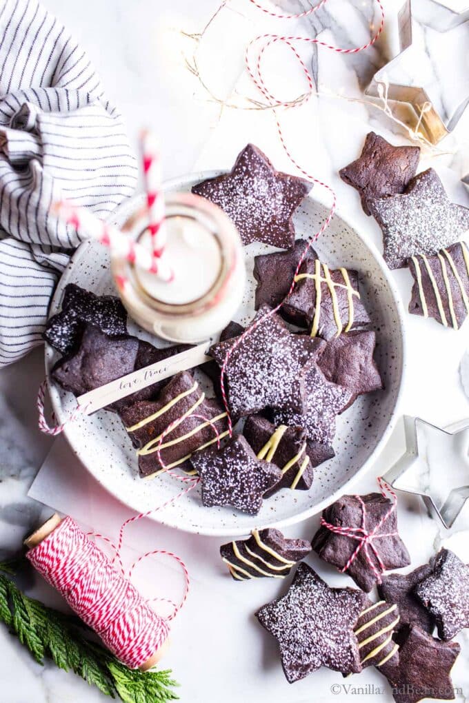 Dark chocolate shortbread cookies cut into stars and decorated on a plate with a glass of milk