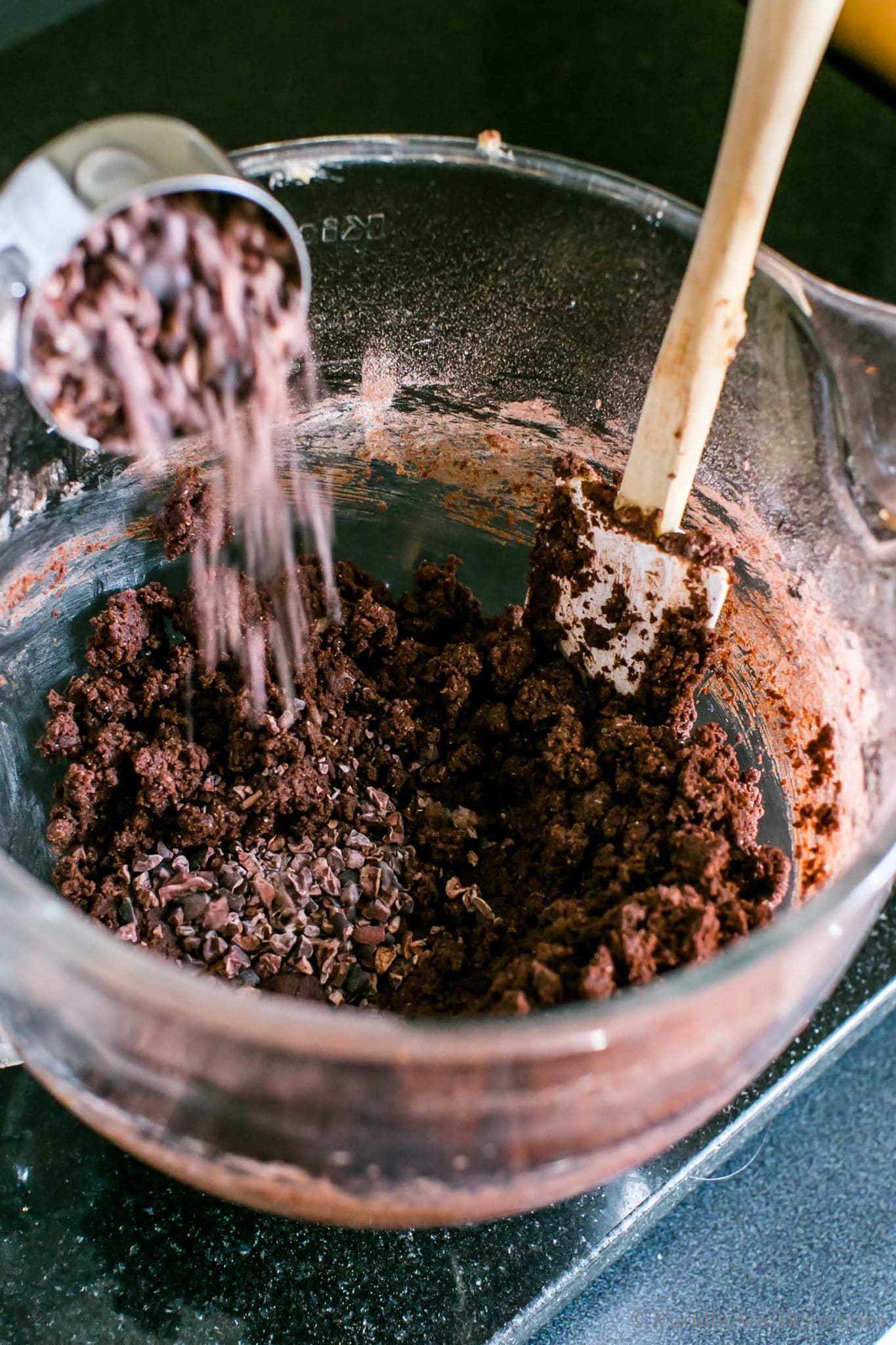 Pouring cocoa nibs into the cookie batter.