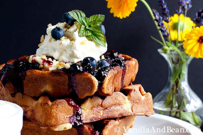 A close up of the waffles topped with blueberries, cream and syrup.