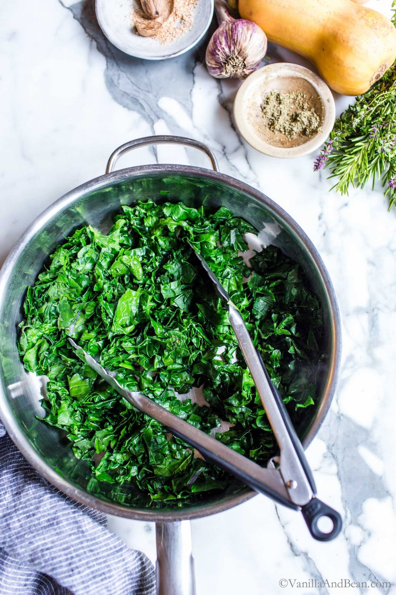 Steamed kale in a pan with tongs.
