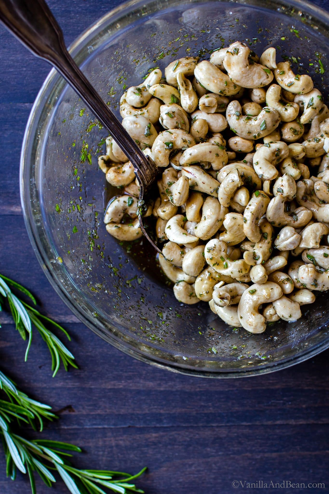 Raw cashews in a bowl tossed with spices, sugar and rosemary. 