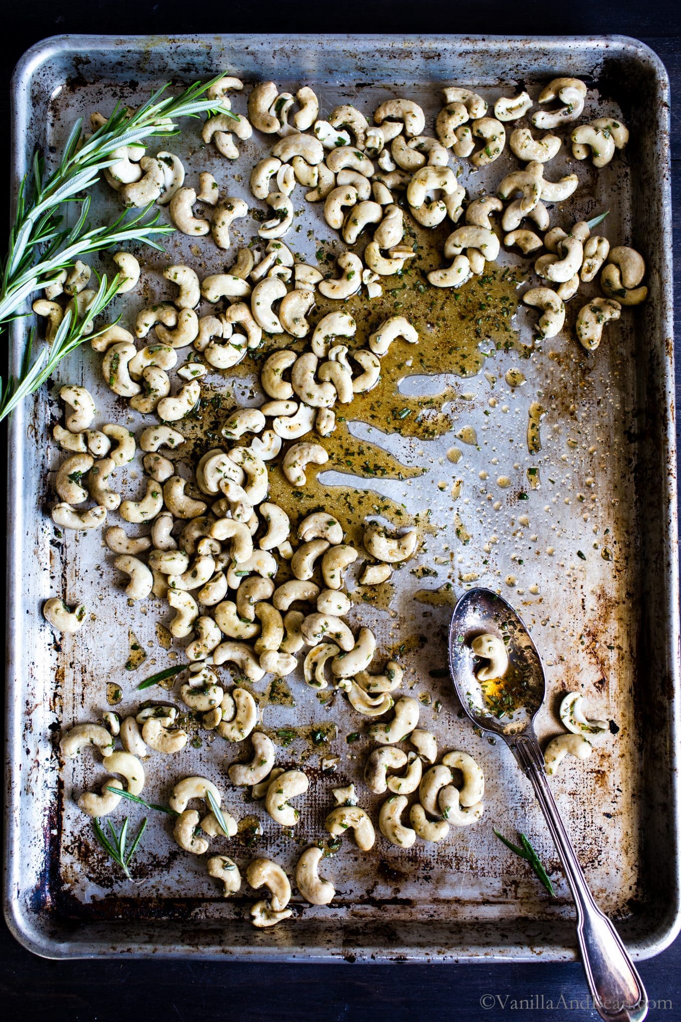 Cashews on a sheet pan tossed with spices, rosemary and sugar ready to be roasted. 