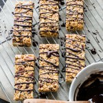 Peanut Butter Fruit and Nut Granola Bars drizzled with chocolate on a wire rack. A bowl of chocolate for drizzling beside the bars.