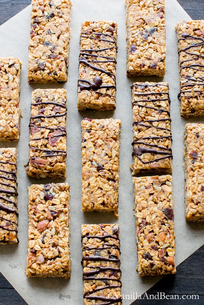Peanut Butter Fruit and Nut Granola Bars on parchment paper. Bars alternating with chocolate-drizzled and non-drizzled ones.