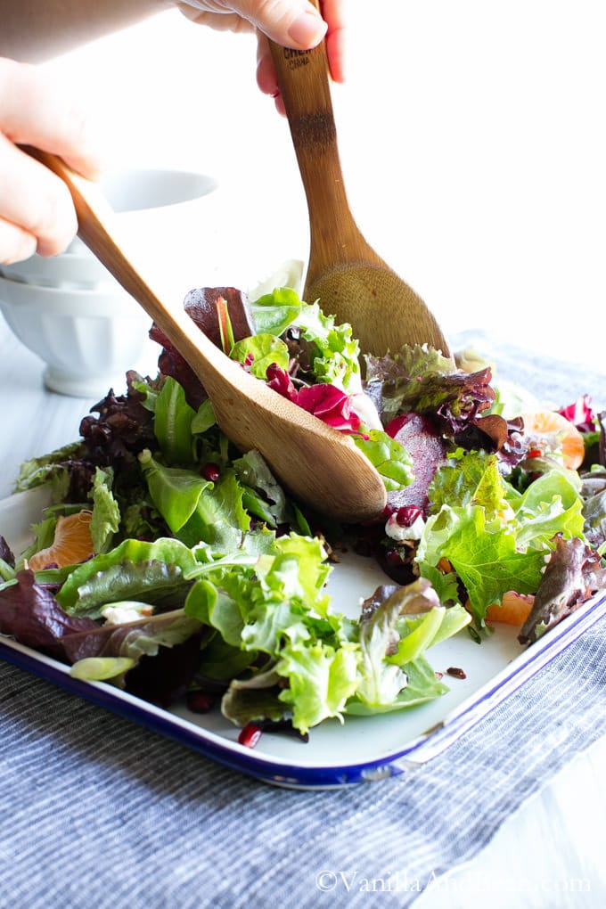 A tray of Winter Jeweled Salad with Citrus Balsamic Vinaigrette tossed with two wooden spoons.
