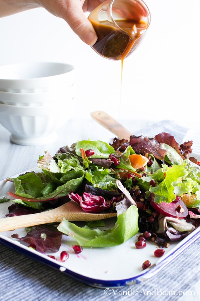 Citrus Balsamic Vinaigrette poured on a tray of Winter Jeweled Salad with two wooden spoons.