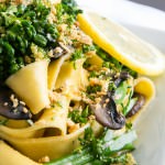 A plate of Pappardelle with Broccolini and Crunchy Gremolata and a slice of lemon.