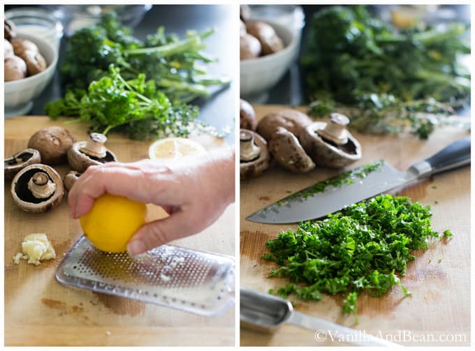 Zesting a lemon with microplane grater surrounded by mushrooms, parsley, and broccolini. Fresh parsley is chopped on a chopping board with a knife.