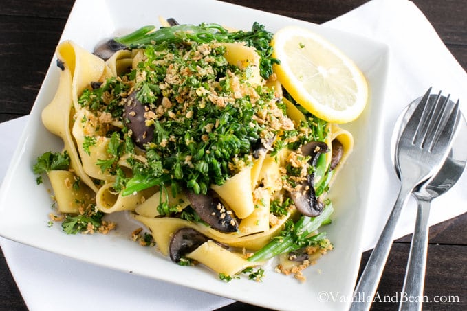 A plate of Pappardelle with Broccolini and Crunchy Gremolata on a table with a spoon and fork.
