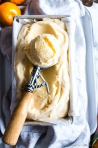 A scoop of orange sherbet in an ice cream scoop.