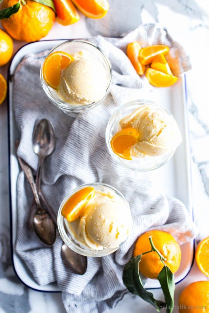 Glass Ice Cream cups holding orange sherbet with spoons on the side. 