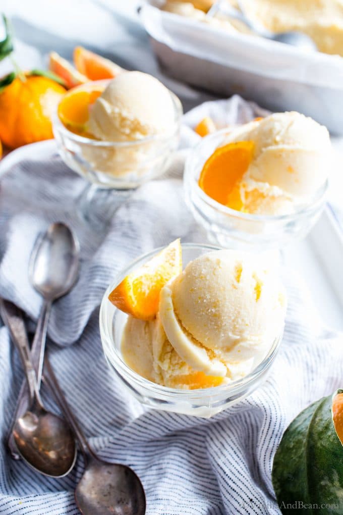 Glass Ice Cream cups holding orange sherbet with spoons on the side. 