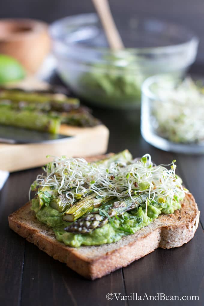 Avocado dip topped with alfalfa and roasted asparagus on a multigrain toast.
