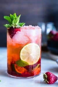 A strawberry mojito garnished with mint, lime and a strawberry.