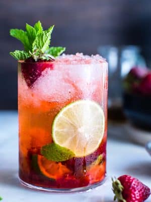 A strawberry mojito garnished with mint, lime and a strawberry.