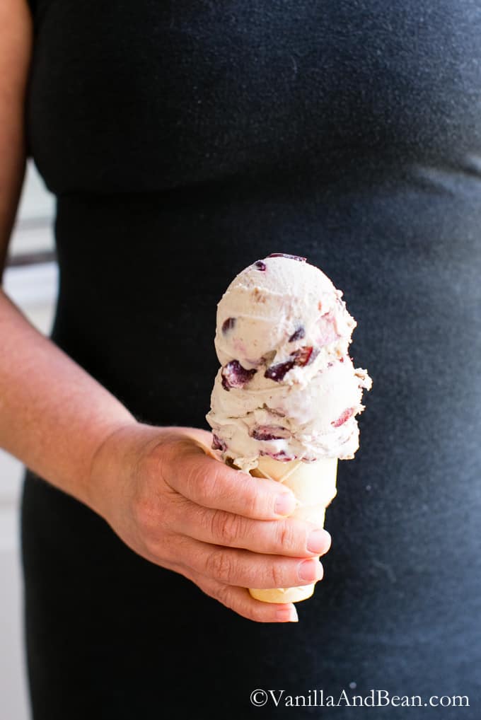 Two scoops of Bourbon Soaked Cherry Vanilla Bean Ice Cream in a cone.