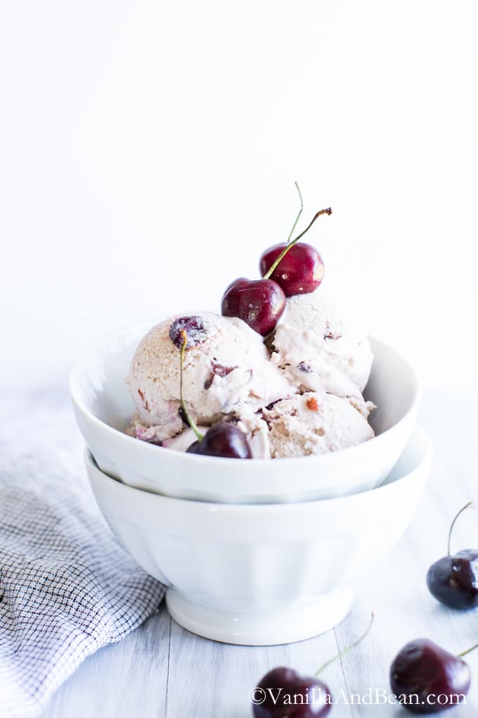 Scoops of the Bourbon Soaked Cherry Vanilla Bean Ice Cream in a bowl topped with fresh sweet cherries.