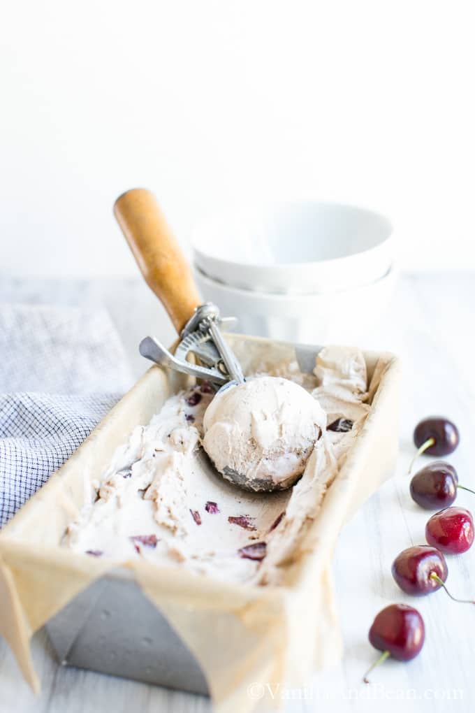 Bourbon Soaked Cherry Vanilla Bean Ice Cream in a loaf pan with an ice cream scoop.