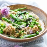 Creamy Farro with Pesto Asparagus and Peas in a flat bowl with a fork garnished with chives and chive flowers.