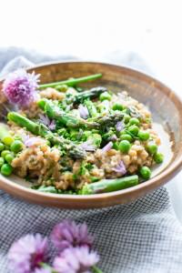Creamy Farro with Pesto Asparagus and Peas in a flat bowl with a fork garnished with chives and chive flowers.