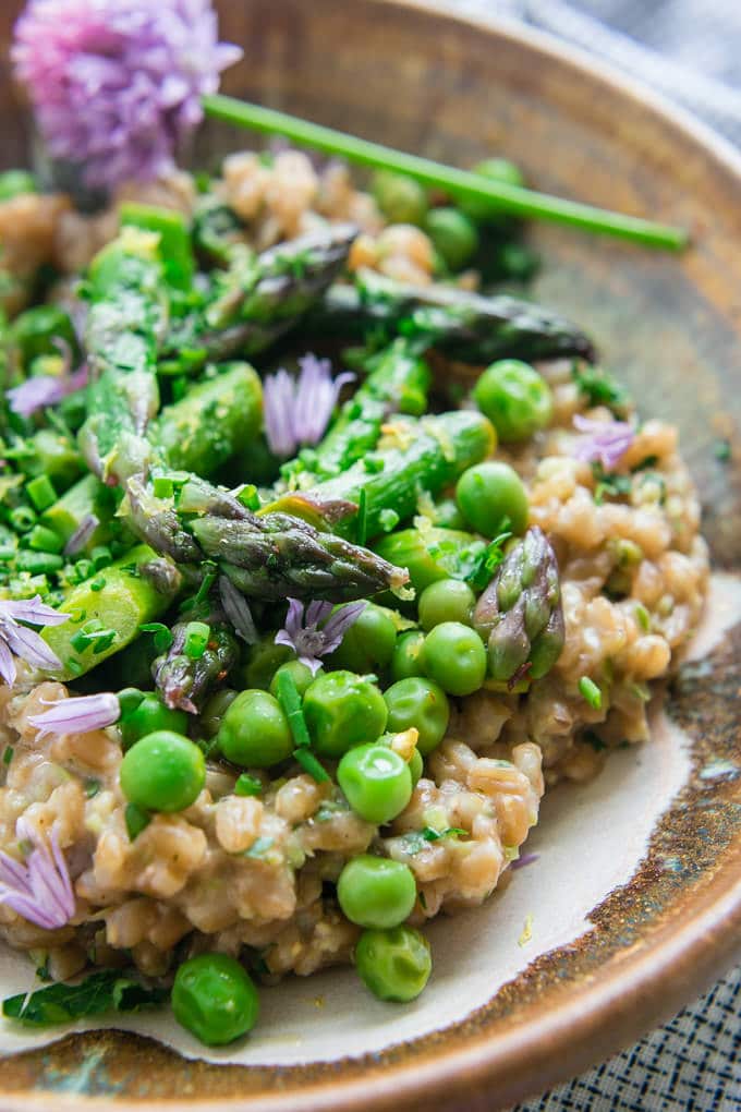 Creamy Farro with Pesto Asparagus and Peas in a flat bowl with a fork garnished with chives and chive flowers. 