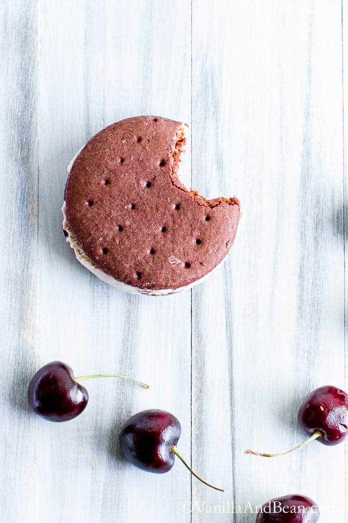 Chocolate Ice Cream Sandwich Cookie with a bite and fresh cherries below it.