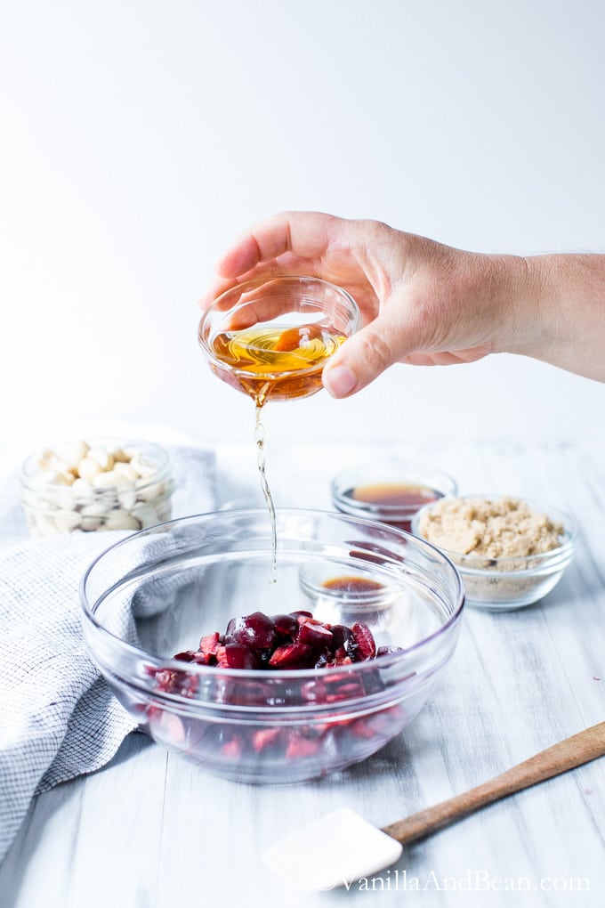 Adding a liquid ingredient to a glass bowl of fresh sweet cherries.