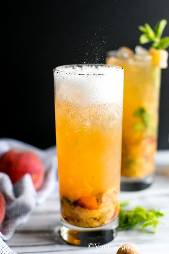 Fizzy Peach Bourbon in a tall glass with another glass of it topped with mint in the background.
