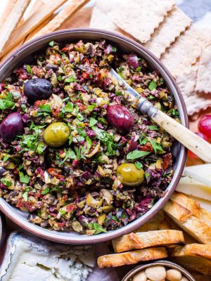 Olive tapenade recipe on a snack board with grapes, almonds, crostini, cheese and breadsticks.