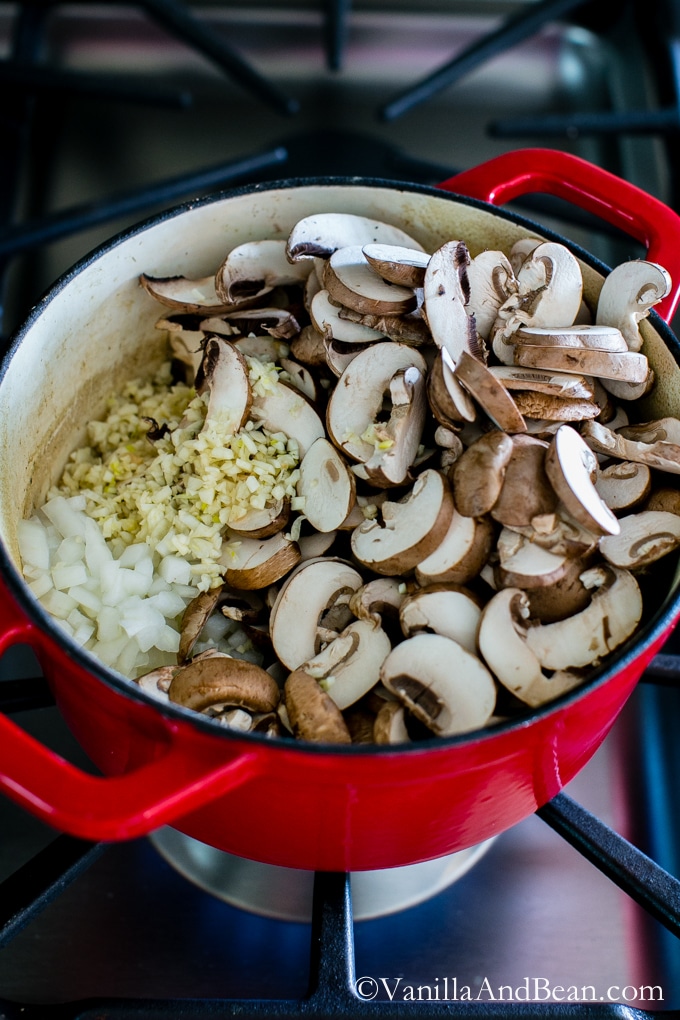 Fresh mushrooms, garlic and onions in a red Dutch oven. 